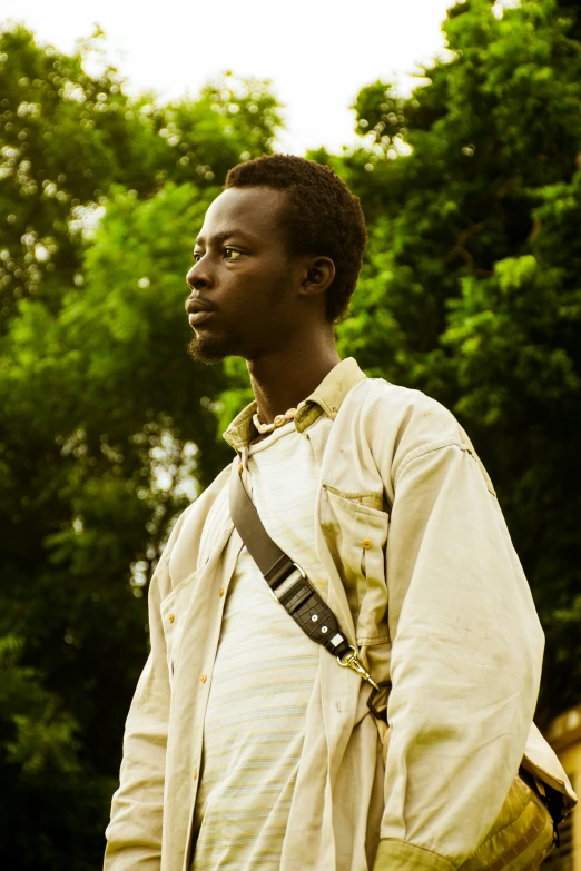 a man with a shoulder bag standing in front of some trees