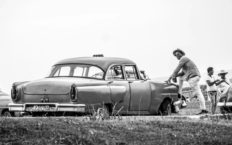 black and white pograph of people looking at old cars