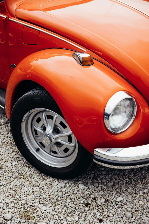 an orange vw bug is parked in gravel