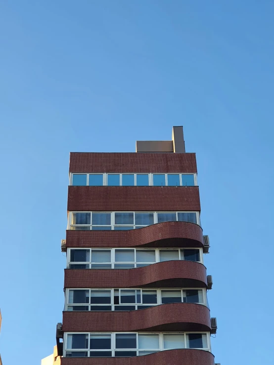 a tall red building with balconies against the blue sky