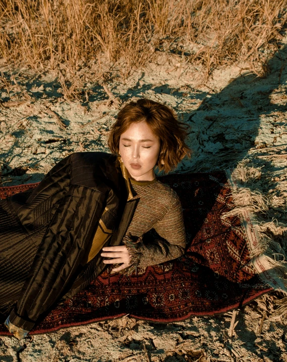 a woman sits on a rug and poses in the grass