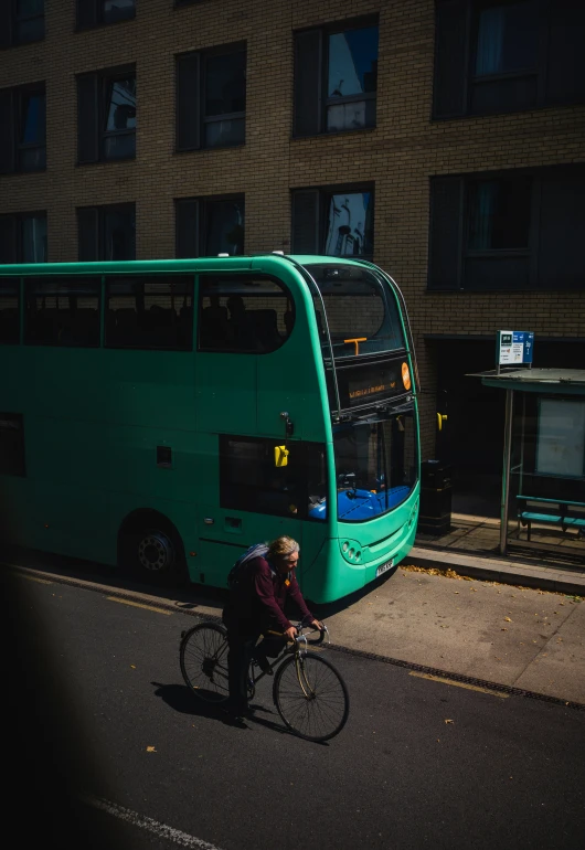 a bicyclist rests at the curb next to a bus