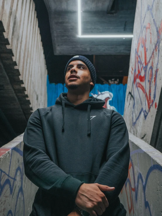 a young man standing in an overpass near graffiti covered wall