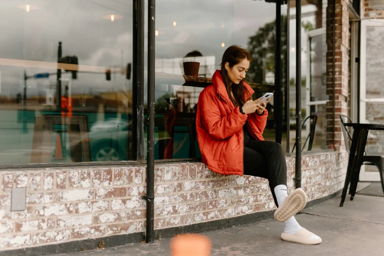 there is a woman sitting outside on a ledge looking at her cell phone