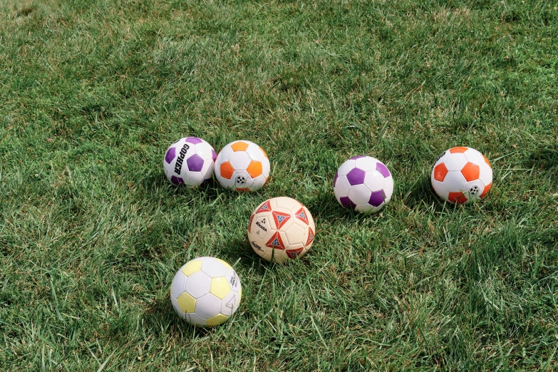 five soccer balls sitting on the grass all together