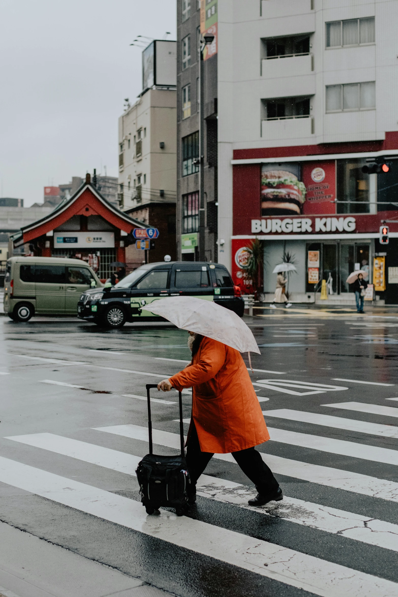 woman in orange with suitcase walking in the rain