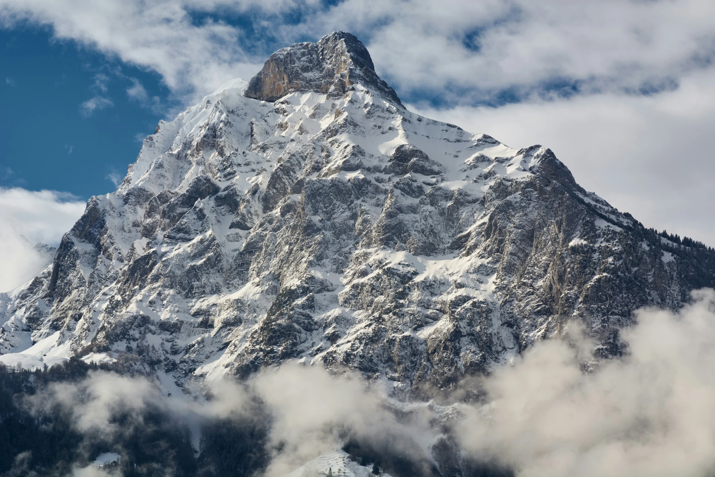 mountains covered in snow and clouds under a blue sky