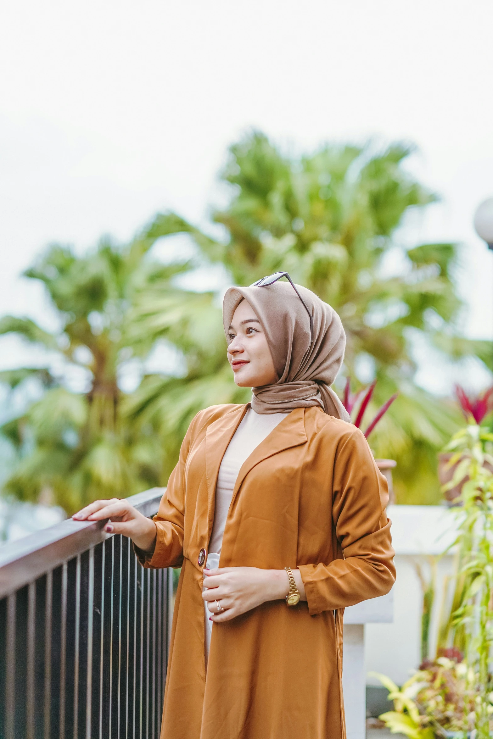 a woman with a hijab and coat standing by a rail