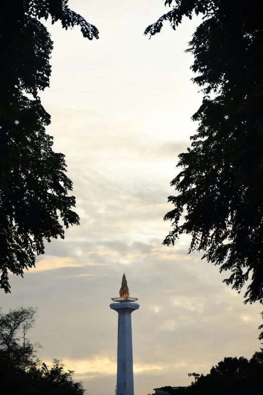 a tall white spire with a red top surrounded by trees