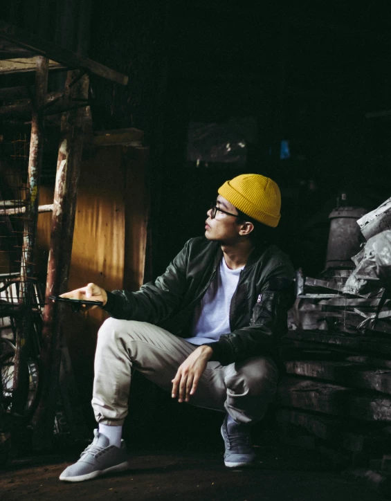 man wearing yellow hat and glasses sitting by stacks of junk