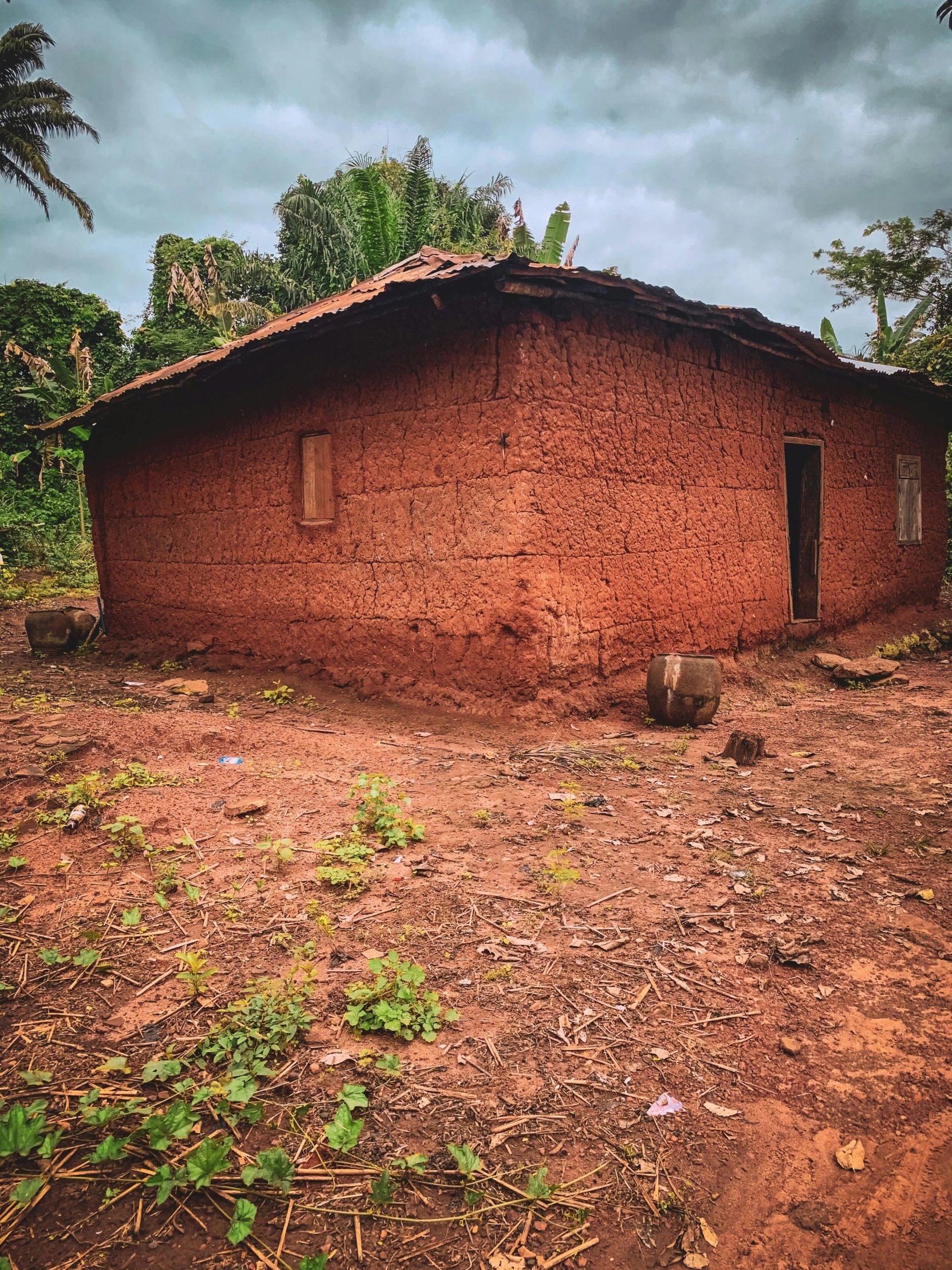 a dirt building with a roof in front of trees