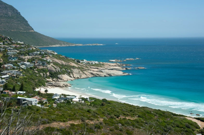 a beach sits between the green hills and the water