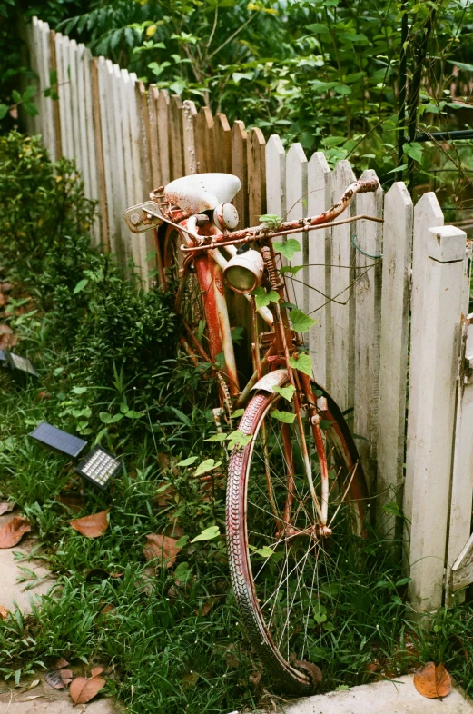an old rusty bike sitting by a picket fence
