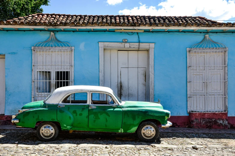 an old green car parked in front of a blue building