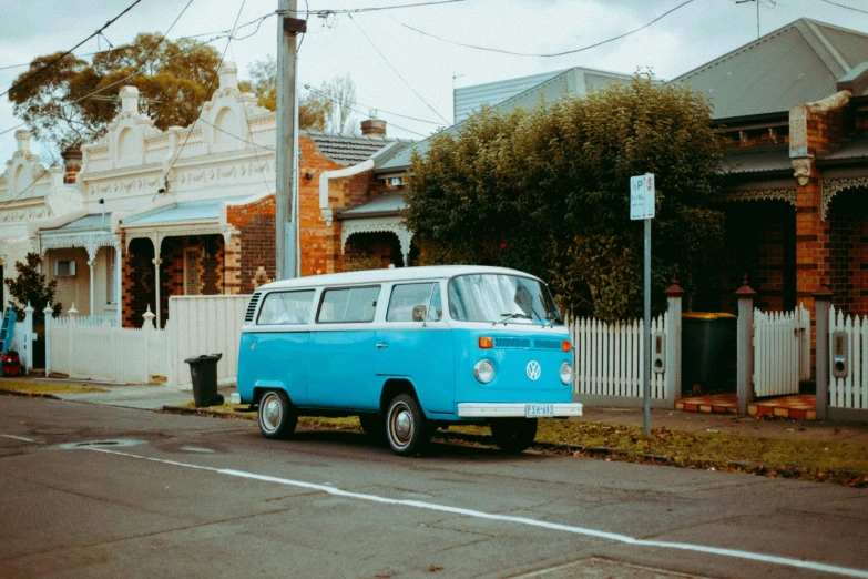 a small blue van on the street next to houses