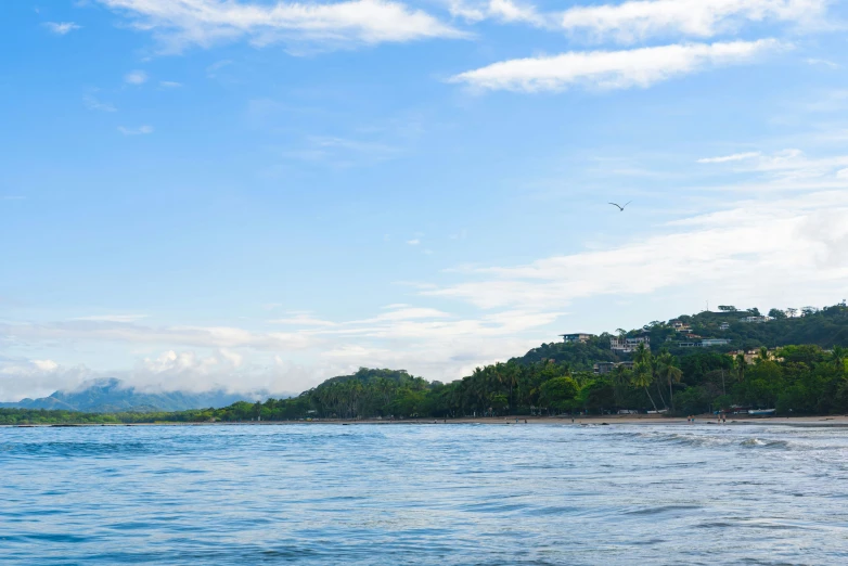 a beach with hills on the shore under a cloudy sky