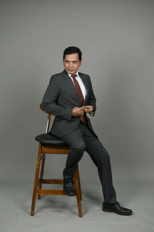 a man sitting on top of a wooden stool wearing a suit