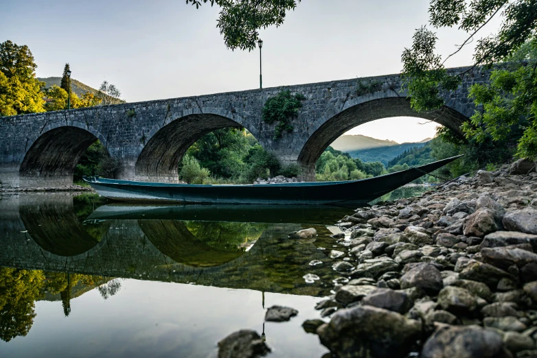 the green boat is going under an old bridge