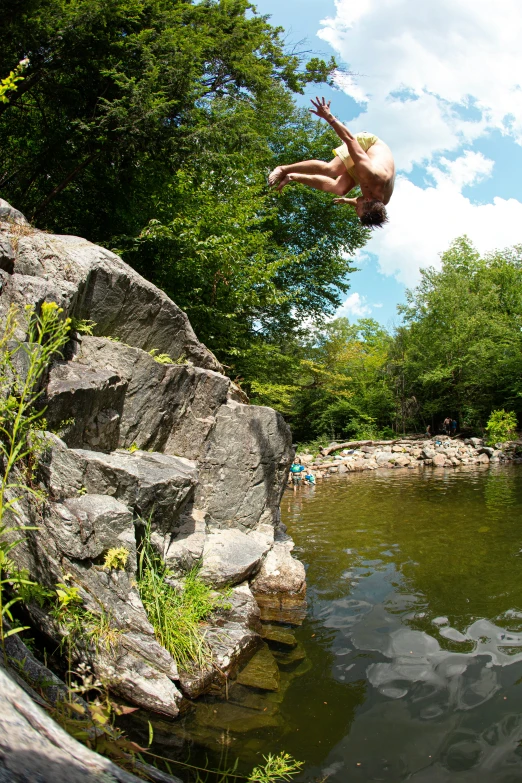 man diving into a pond from the cliffs of a park