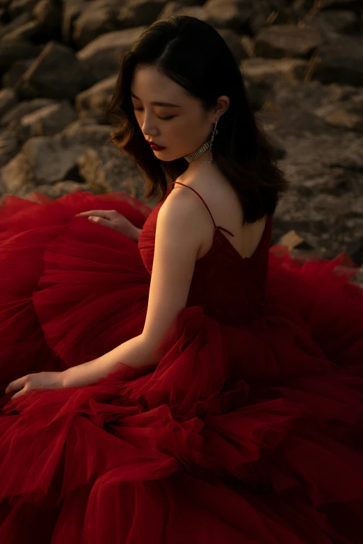 woman in red gown sitting on rocks with hand on hips