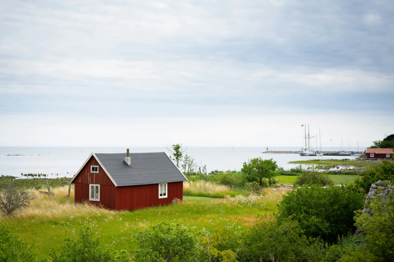 the small house has a black roof in a field by the ocean