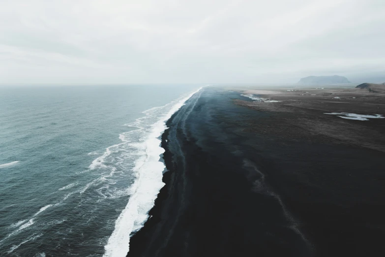 ocean view with cliffs, a gray sky, and black sand