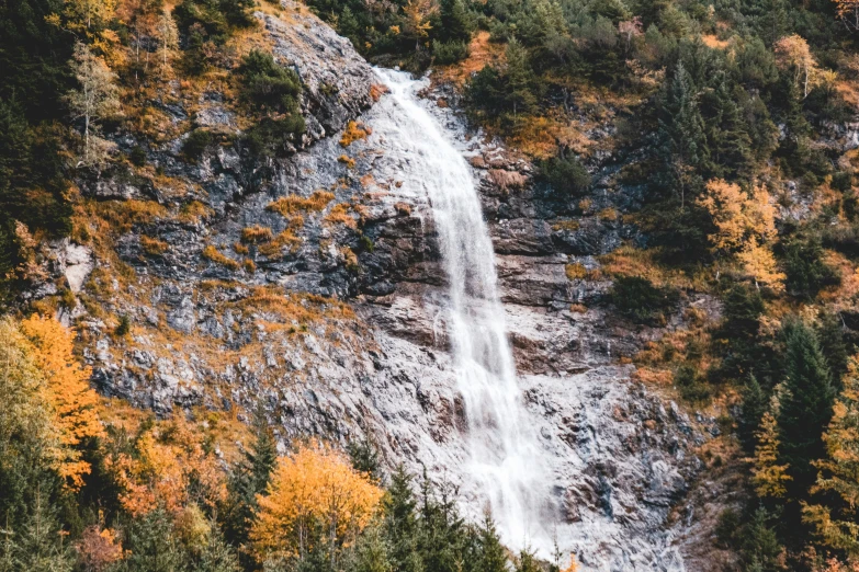 a waterfall in the mountains surrounded by colorful autumn trees