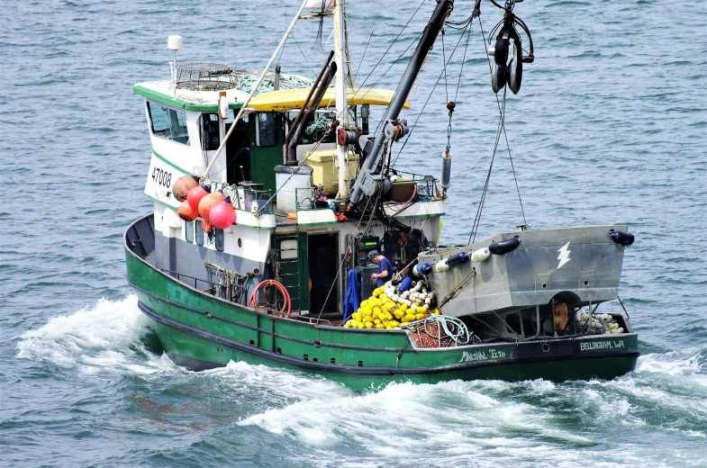 a green and white fishing boat traveling across the ocean