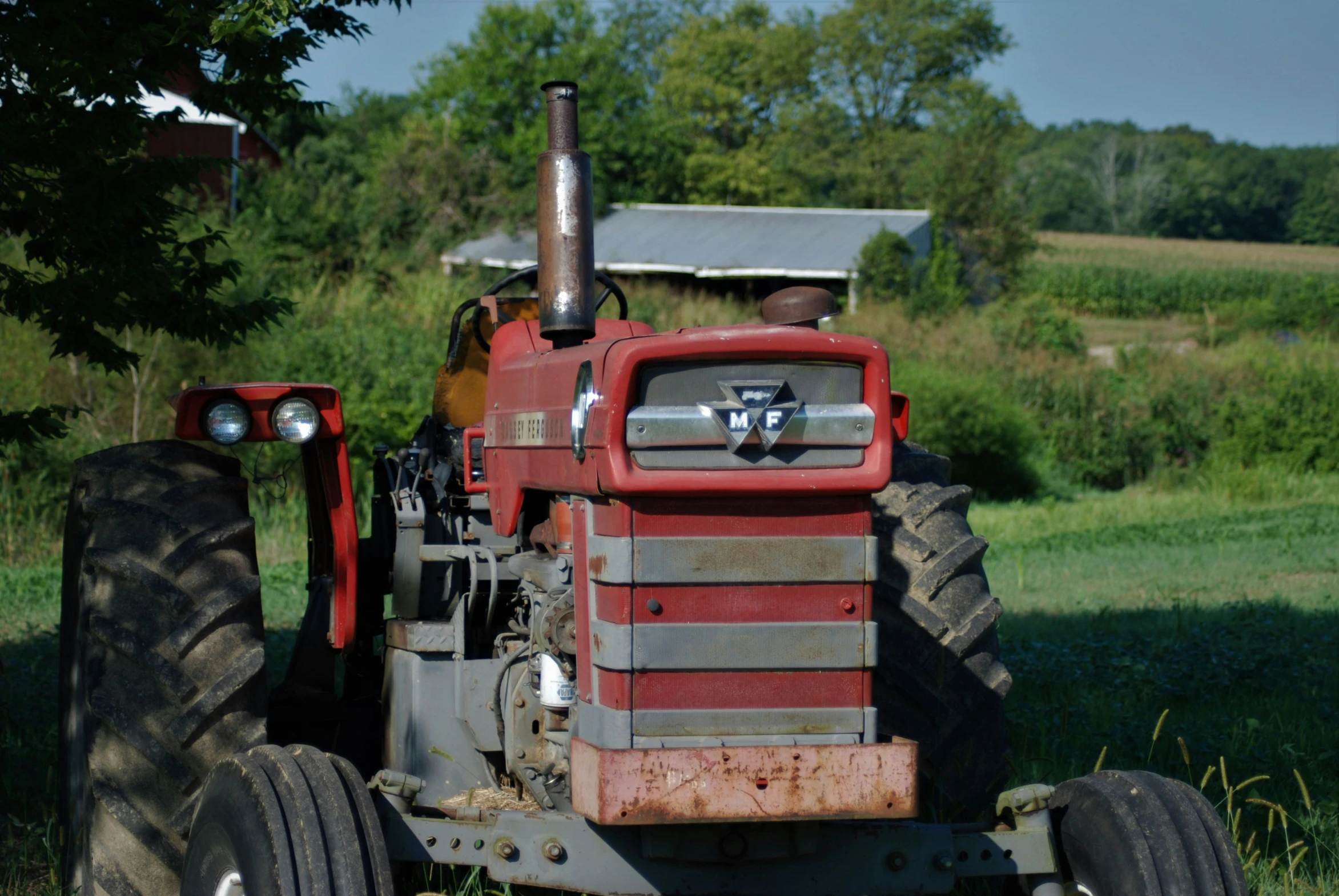 an old tractor sits in the grass near trees