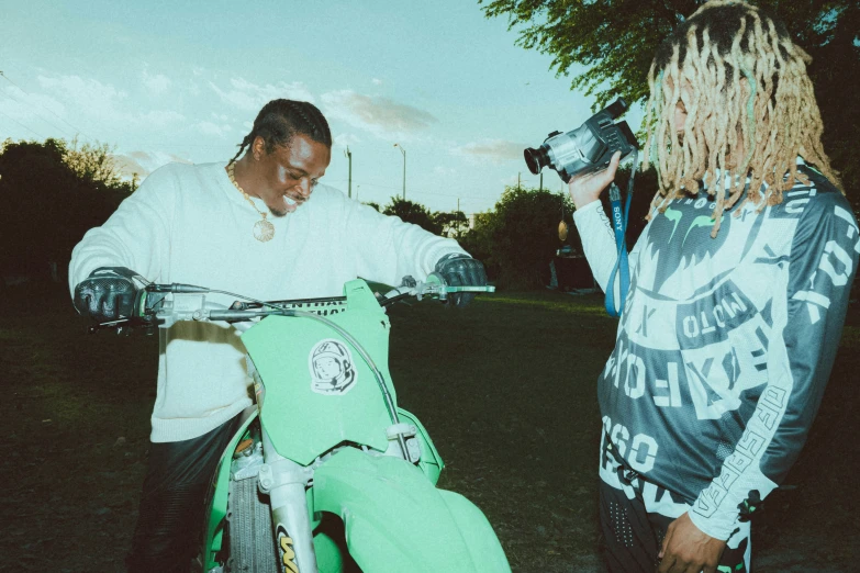 two black men in grass with their green motorbike