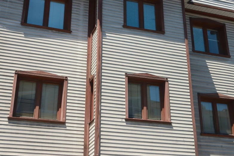 two windows with wood trim on the side of a white house