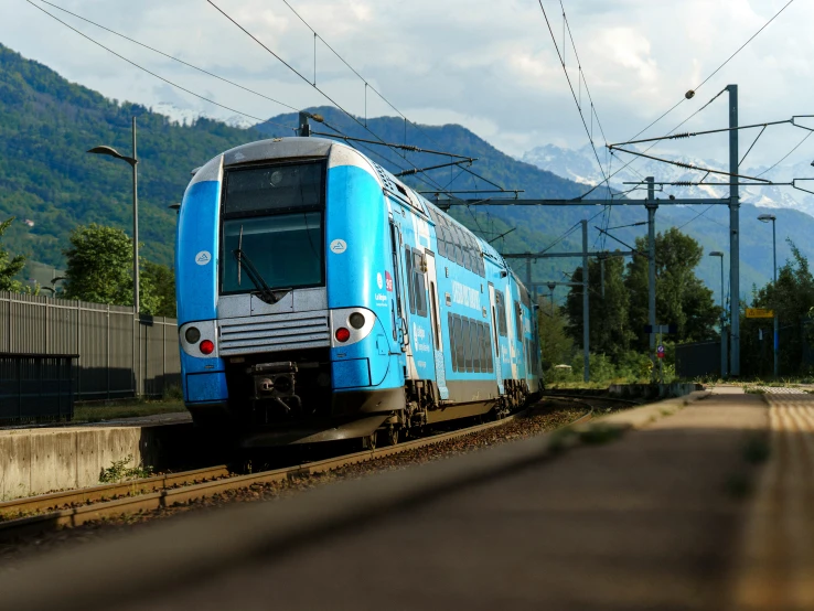 blue commuter train traveling down the tracks in a mountainous setting