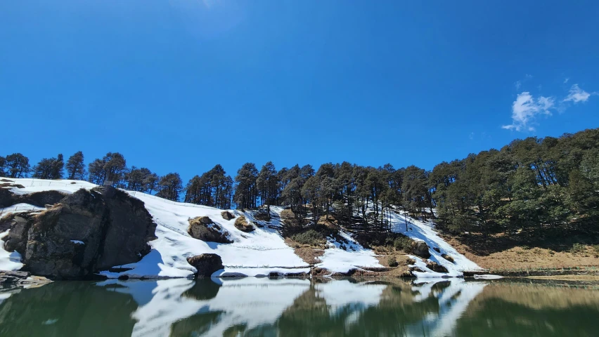 snow on the top of some rocks in front of a lake