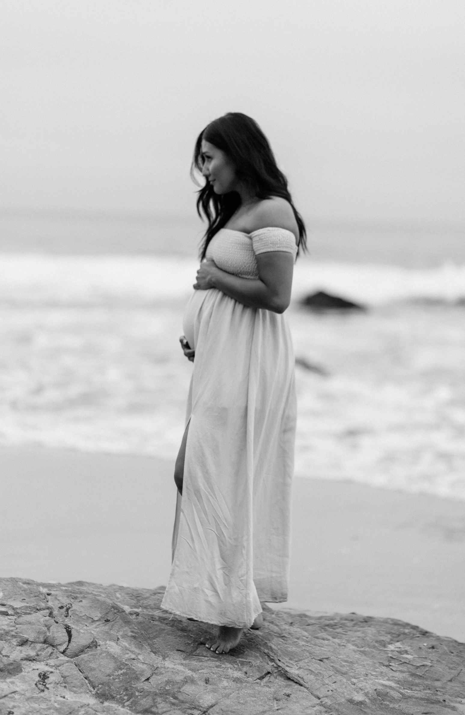 a pregnant woman is standing on a rocky coast