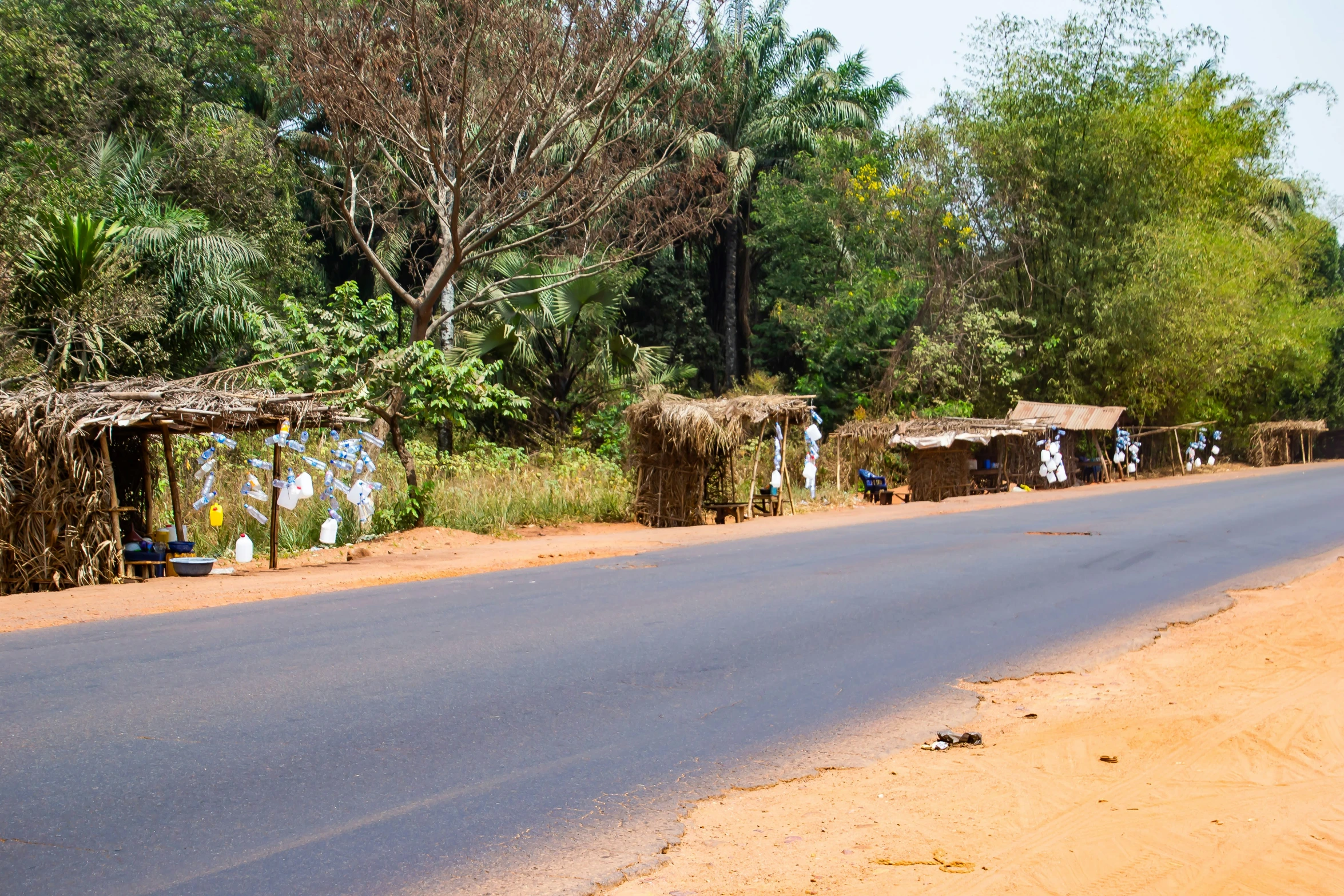 an empty road with two shacks on both sides and trees surrounding