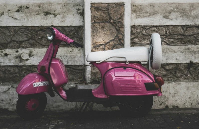 a pink scooter parked outside of a brick wall