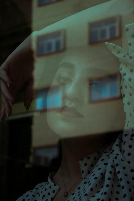 woman with polka dot shirt standing behind glass window with large face