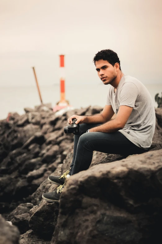 a man sitting on some rocks next to the water