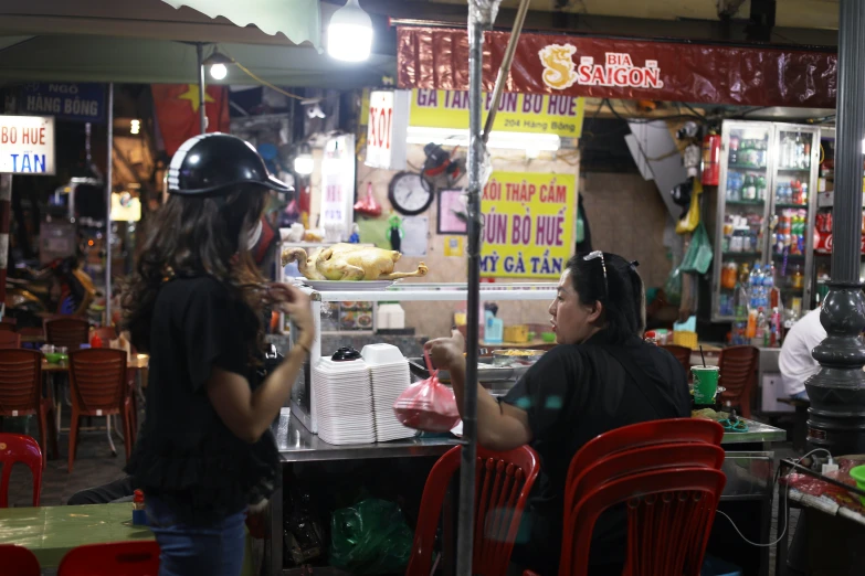 two women sitting at an outdoor food stand