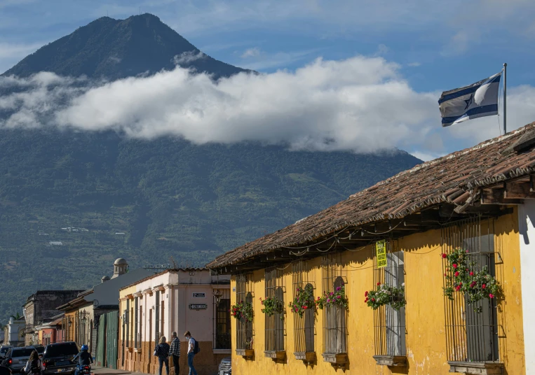 a group of people are walking on a street past houses with a mountain in the background