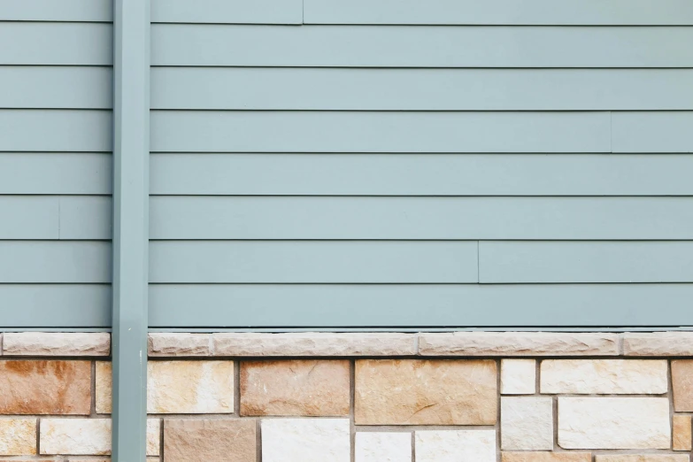 a brick planter with green weeds on the corner next to a gray and beige wall