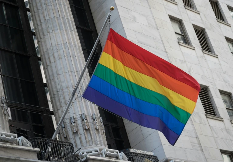 a multicolored gay pride flag hanging off the side of an old building