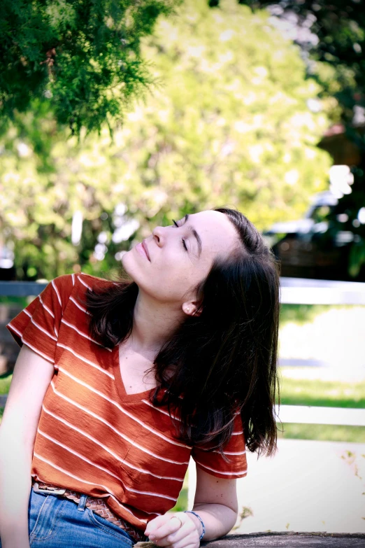 a young woman sitting on the ground while looking up at a tree