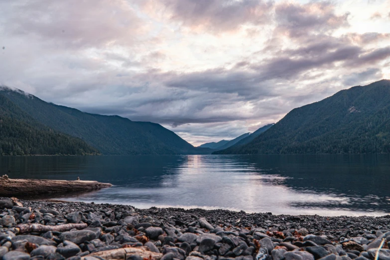 rocks sit on the shore of a lake with mountains in the background