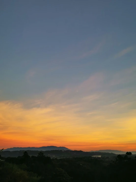 the sun is set in the horizon with mountains and trees in the background