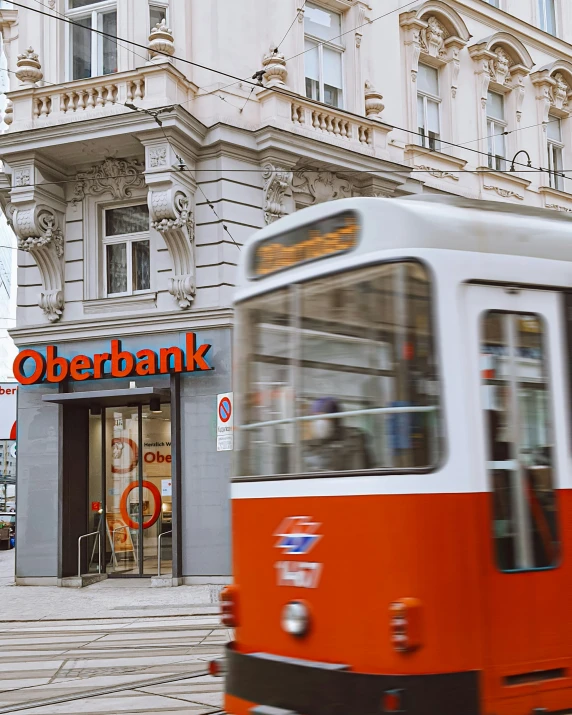 the orange and white bus is going past a bank