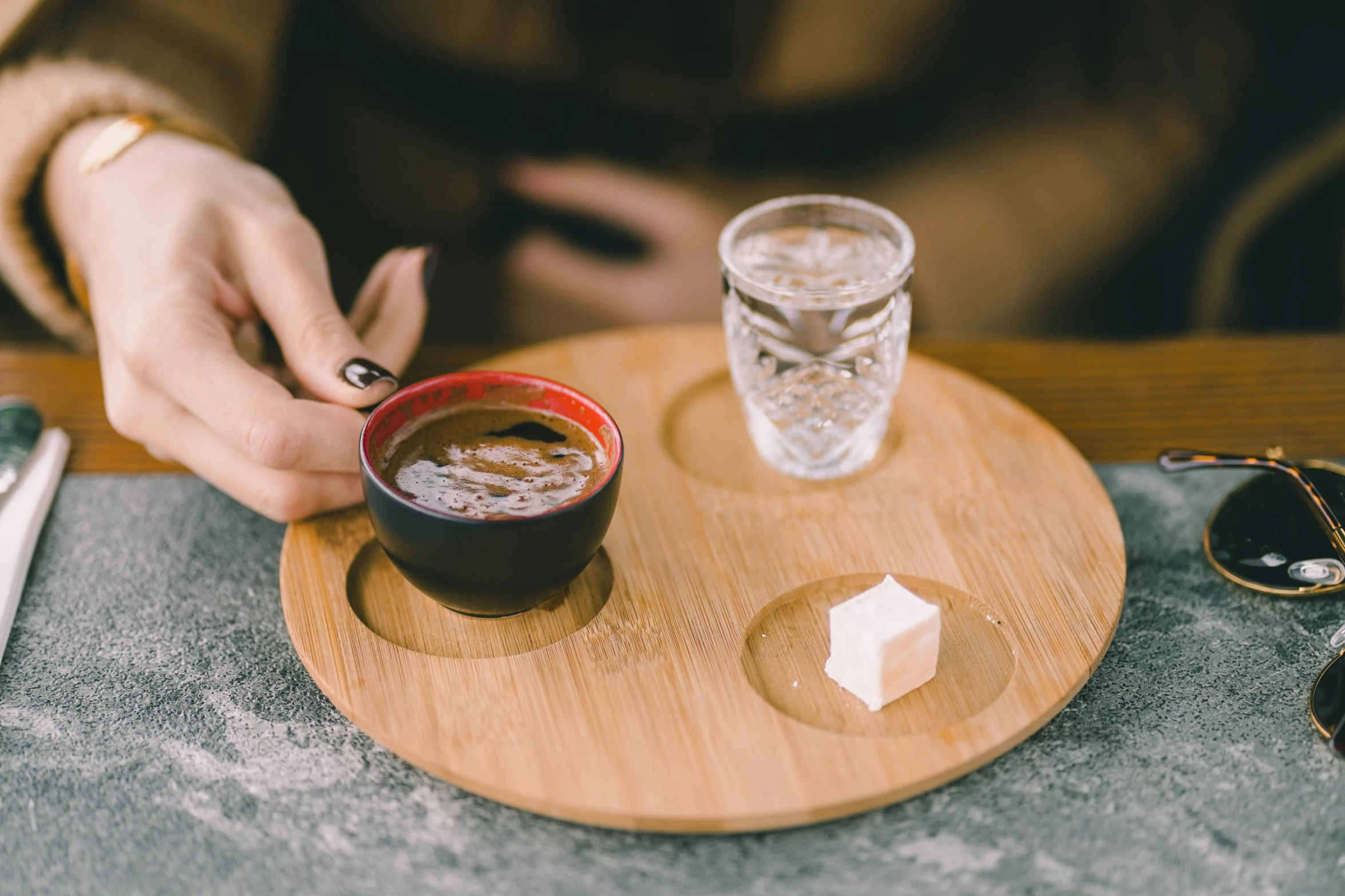 a woman holds her nails while a cup of coffee and ice are on the table