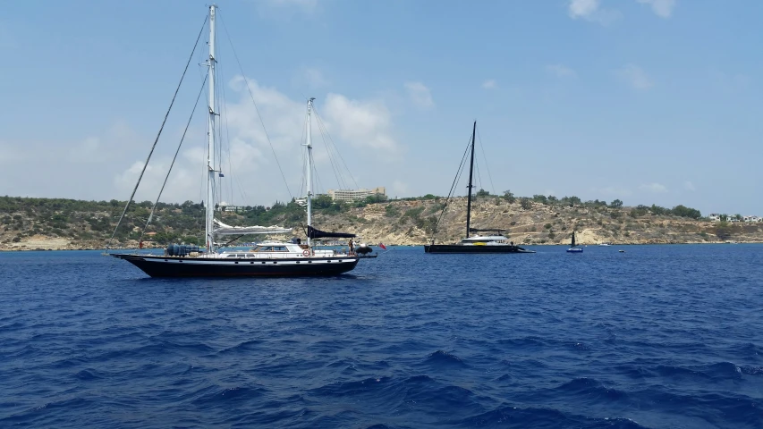 three sailboats on calm blue water with an island in the distance