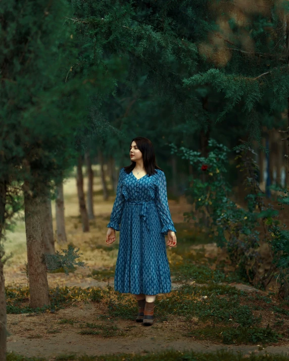 a woman in a blue dress standing in a wooded area with trees