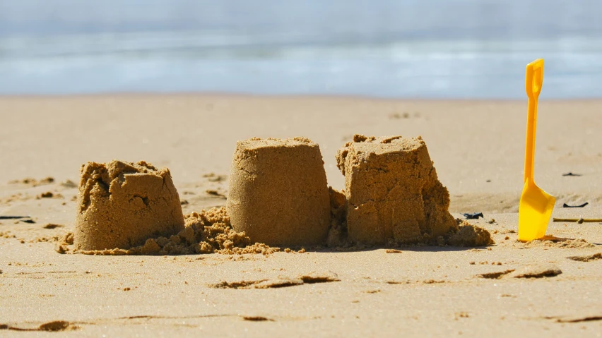 some sandcastles in the sand with one shovel next to them